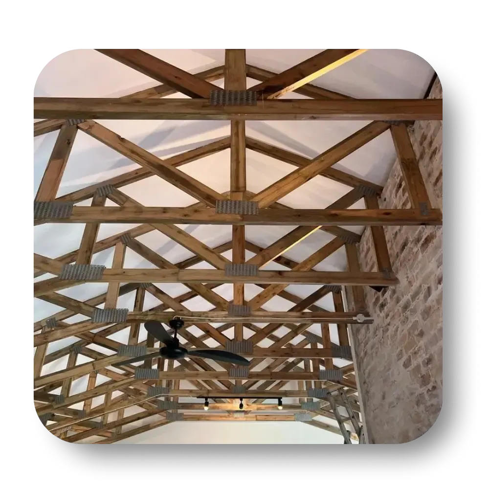 Wooden rafters and trusses in a ceiling with exposed support beams, a ceiling fan, and brick wall.