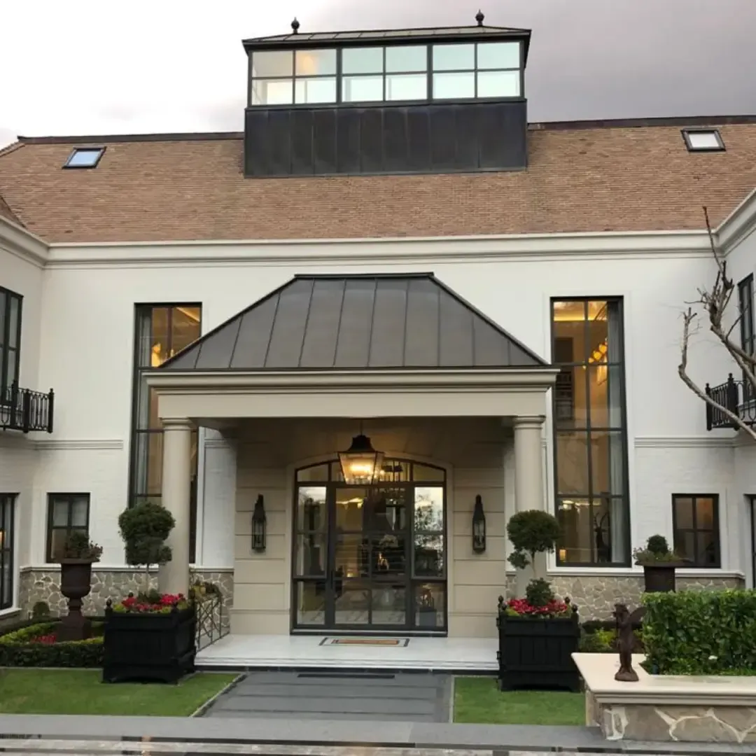 Elegant white building entrance with a dark metal roof and large glass doors.