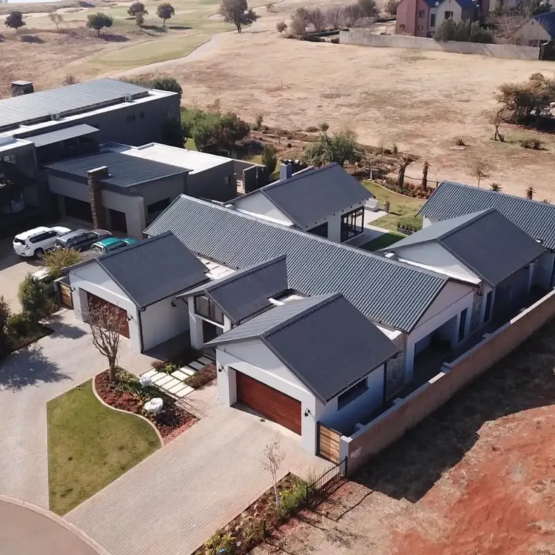 Aerial view of modern homes with gray roofs and white walls, set against a dry, brown landscape with some greenery.