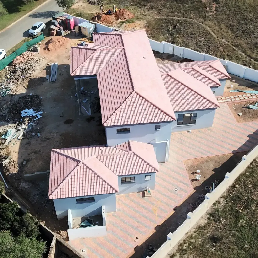Brick homes with orange tiled roofs under construction. White truck parked nearby.