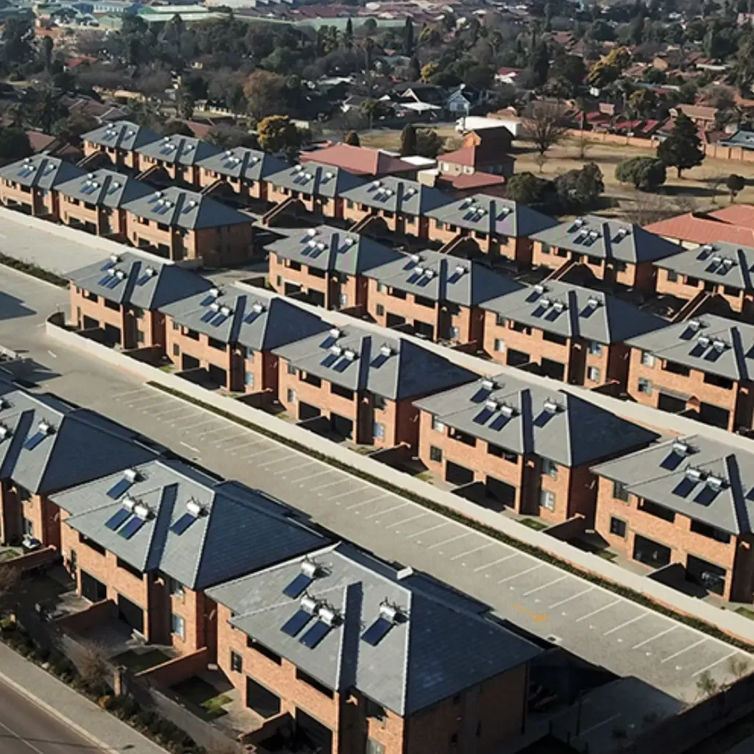 Aerial view of a residential complex with rows of brick houses and gray rooftops; parking spaces are visible.