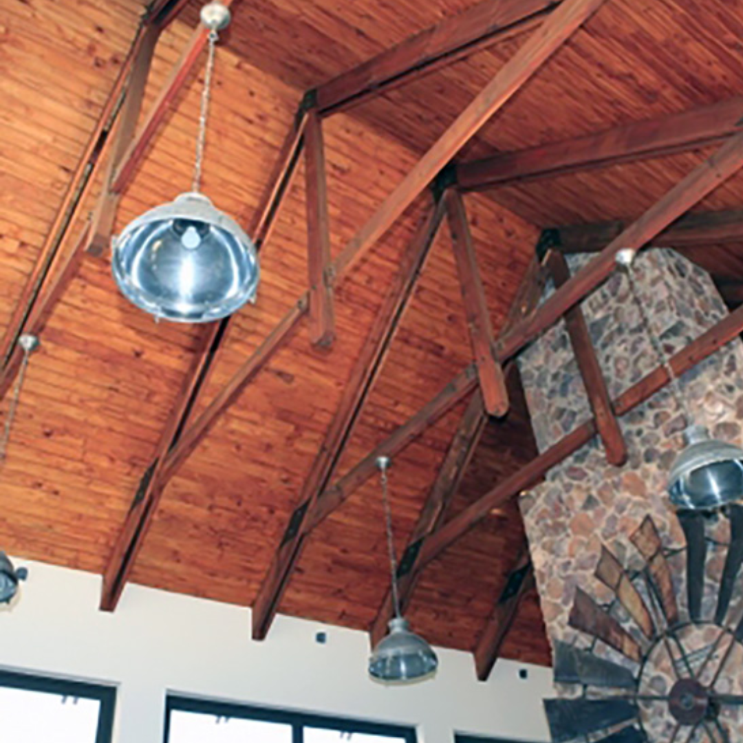 Wooden ceiling with exposed beams and pendant lights, a stone fireplace, and a decorative metal piece.