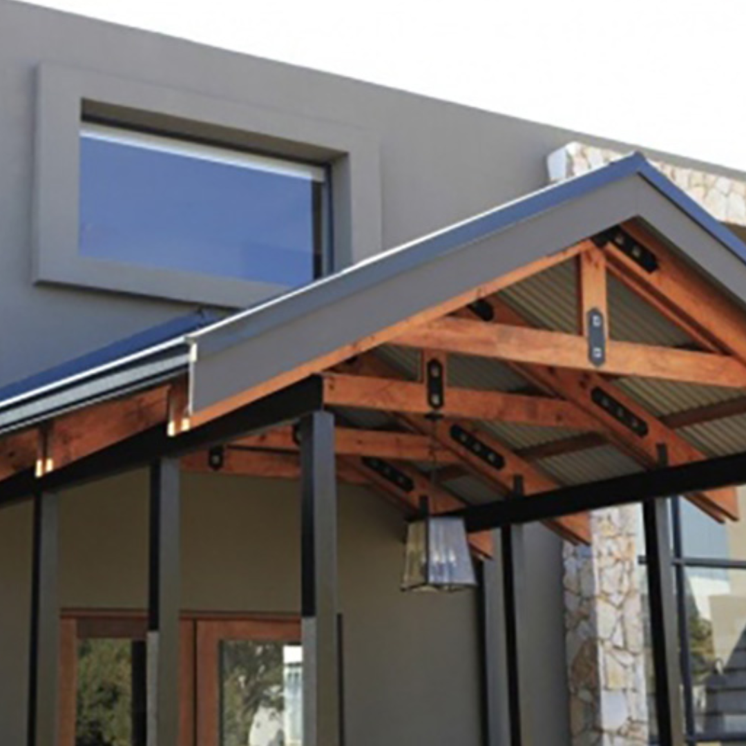 Wooden porch with a metal roof, attached to a gray building with a window and a stone facade.