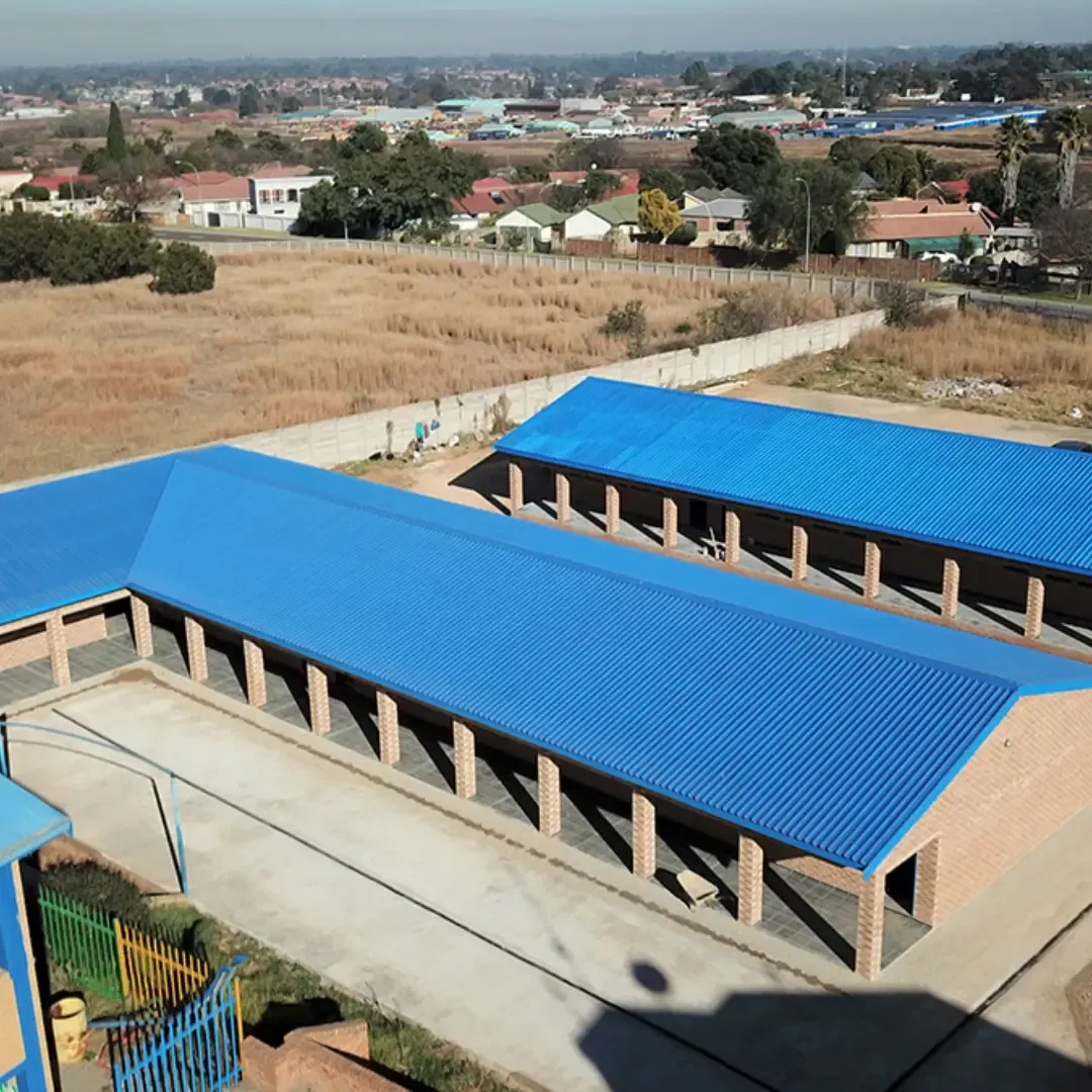 Blue-roofed school buildings with brick pillars in a sunny setting, viewed from above.
