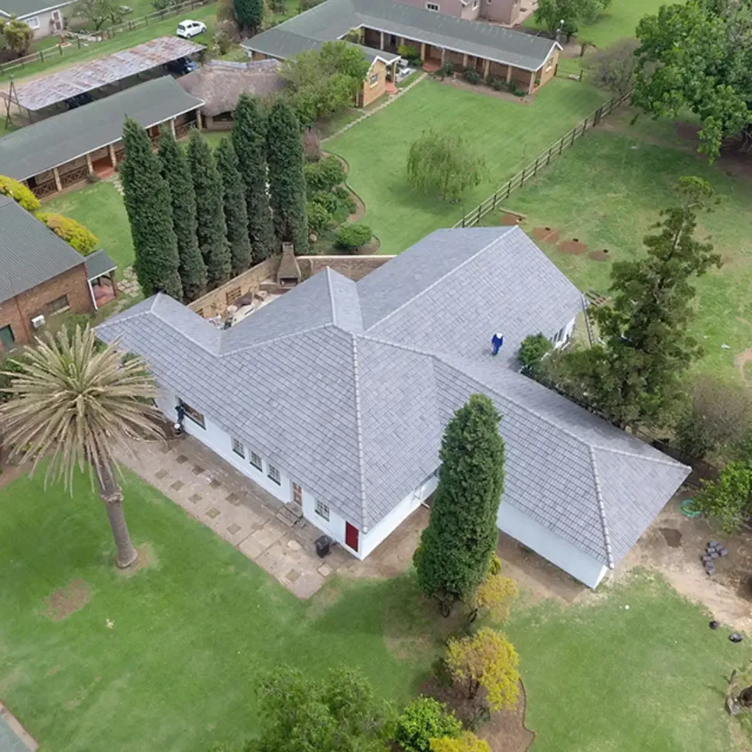 Aerial view of a white building with a gray roof, surrounded by green grass and trees.