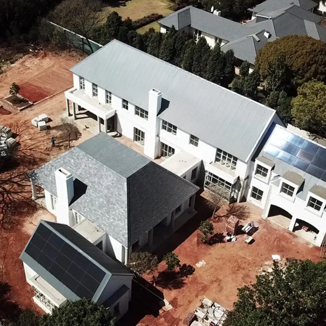 Aerial view of large white houses with gray roofs, solar panels, and surrounding landscaping.