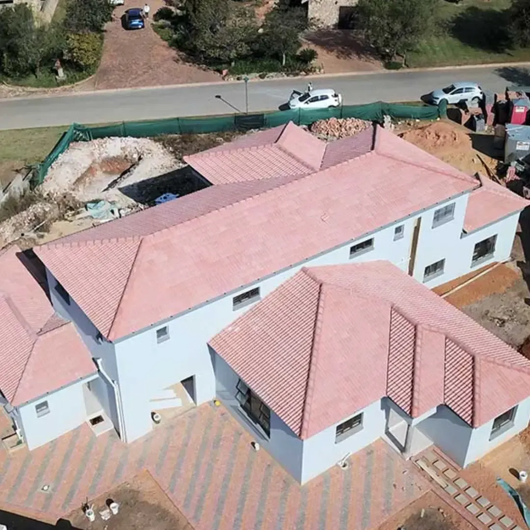 Aerial view of a light-colored two-story house with a red tiled roof under construction, in a residential area.