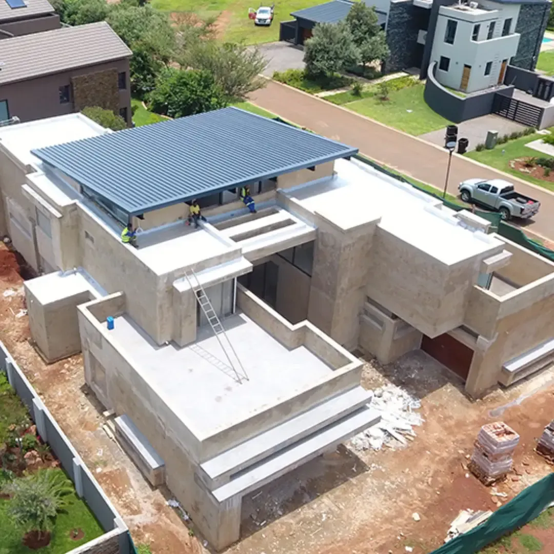 Modern house under construction, with flat roofs, workers, and blue sky.