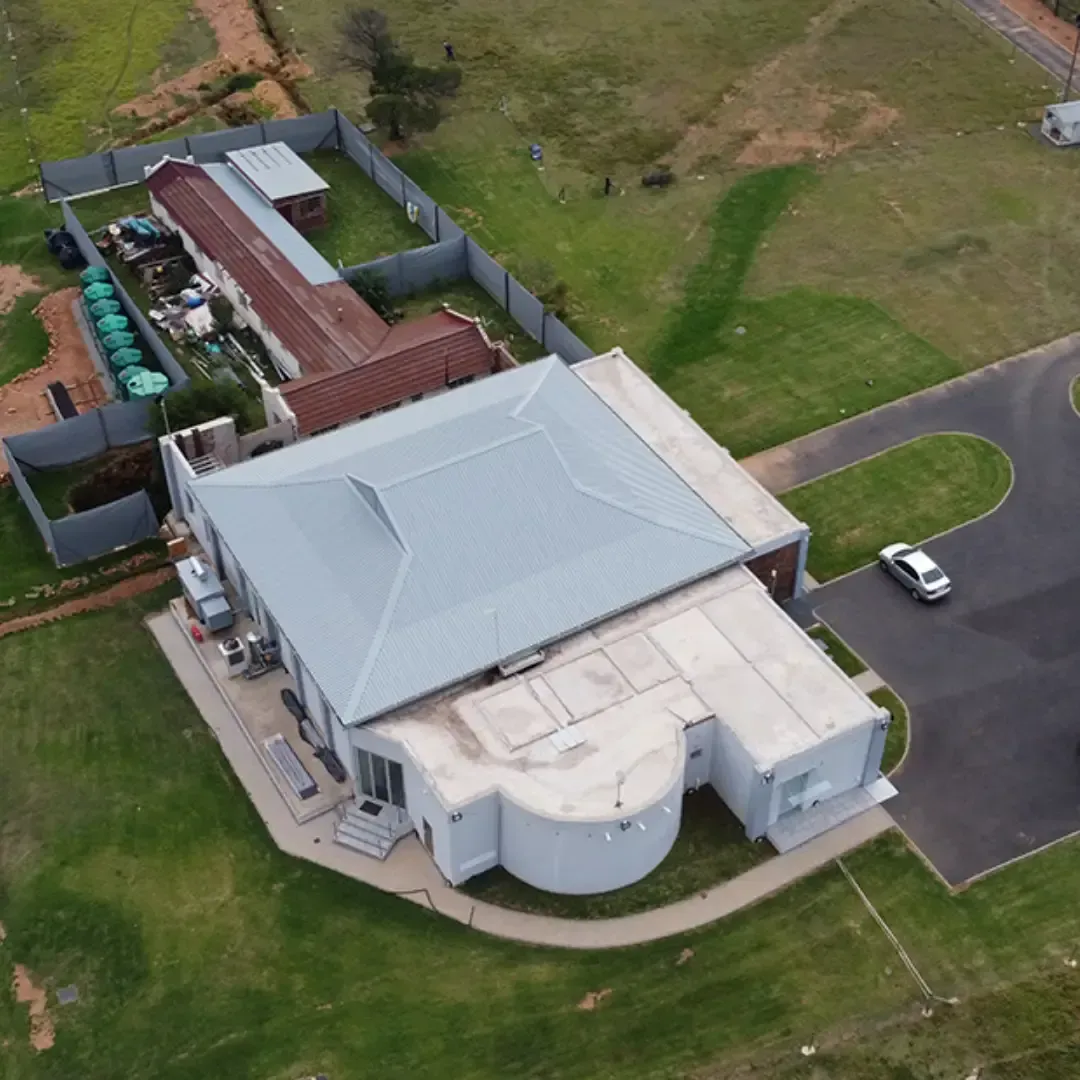Aerial view of a modern house with a car in the driveway and another building in the backyard on a green lawn.