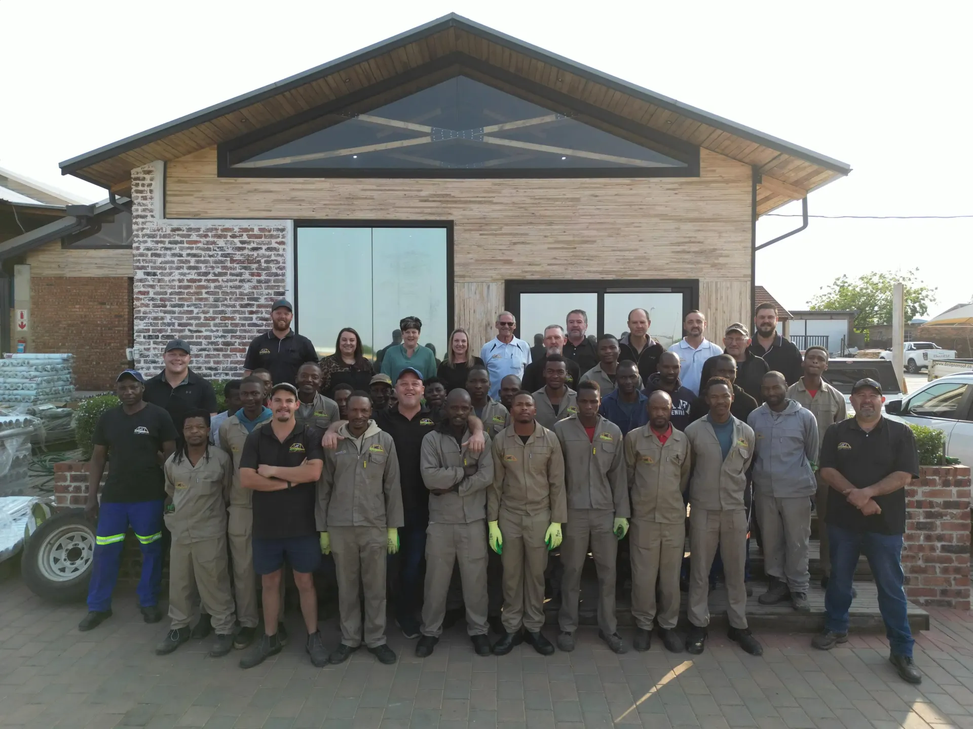 Group of people posing in front of a building. Many wear work clothes. Day time.