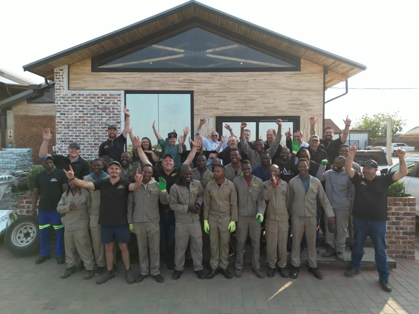 Group of workers celebrating in front of a brick building, arms raised.