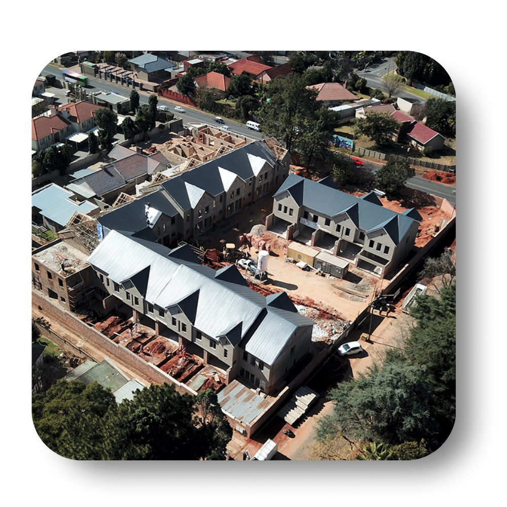 Aerial view of townhouses under construction in a residential area; dirt, brick, and gray roofs.