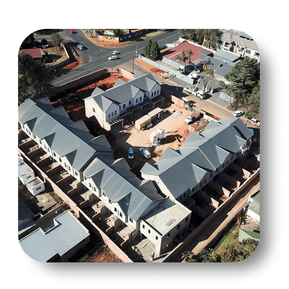 Aerial view of a multi-unit housing complex under construction, featuring gray roofs and surrounding roads.