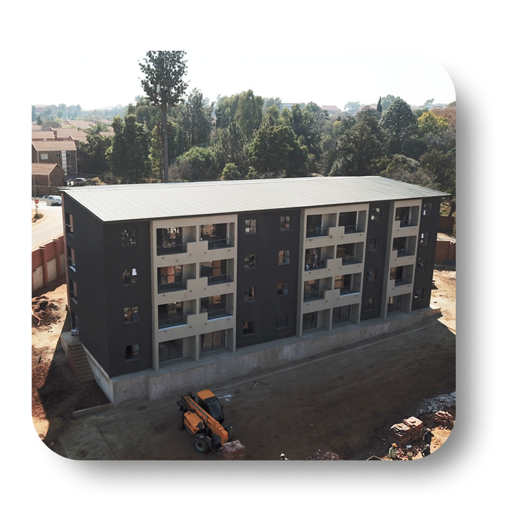Three-story apartment building with dark facade, balconies, and construction equipment in front.