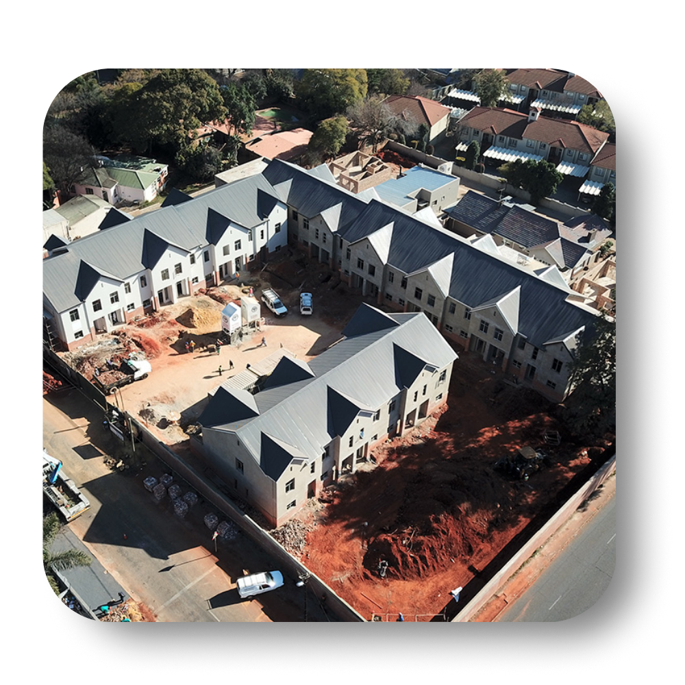 Aerial view of new townhouses under construction with gray roofs and red soil.