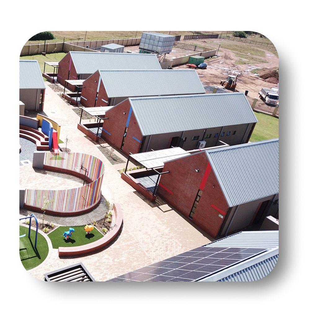 Aerial view of several red brick buildings with gray roofs and playground area.