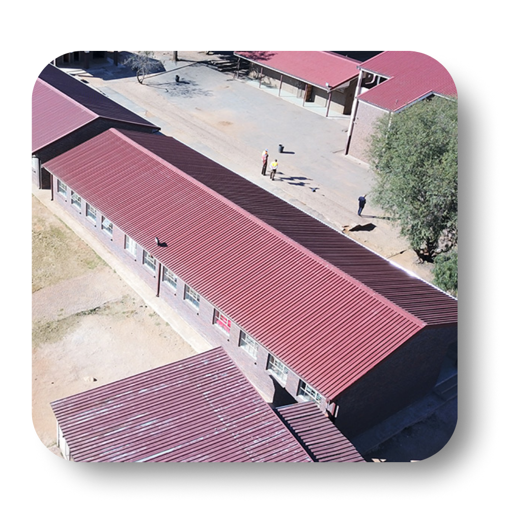 Overhead view of a building with a long, red roof. People walk on a dirt path outside.