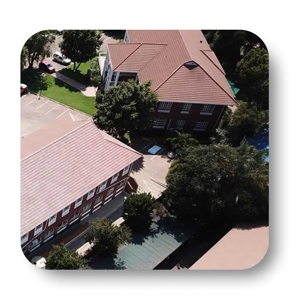 Aerial view of a brick building with a red tile roof surrounded by green trees and grass, and parking lot.