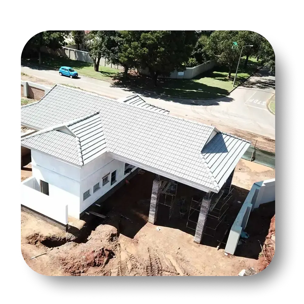 Aerial view of a modern white house under construction with a gray roof and blue car driving by.
