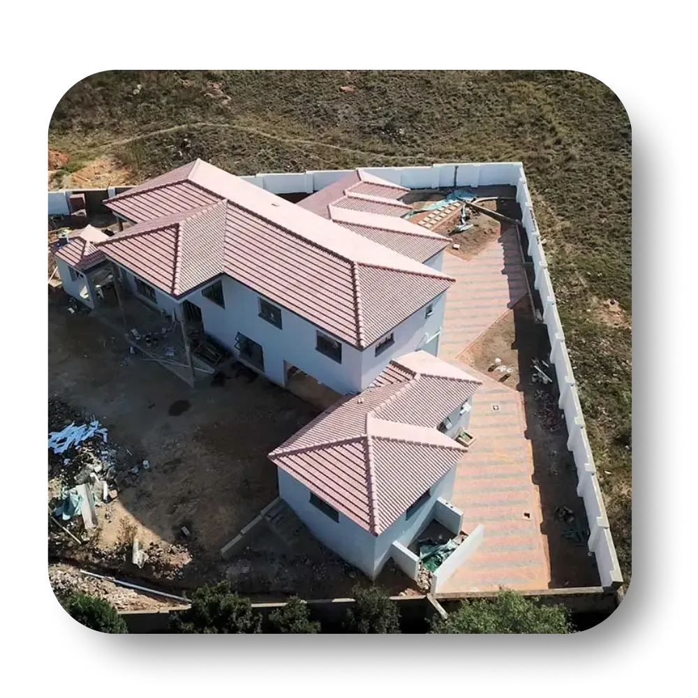 Aerial view of a house under construction with a red tile roof, fenced yard, and brick driveway.