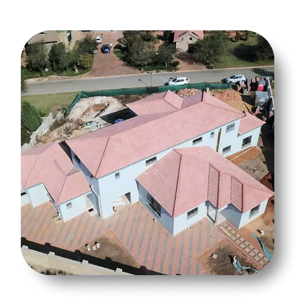 Aerial view of a multi-level house under construction with red tile roof, on brick paved area.