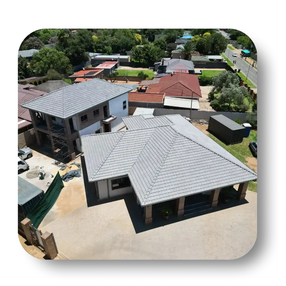 Aerial view of homes with gray tile roofs, surrounding neighborhood with green trees, blue sky.