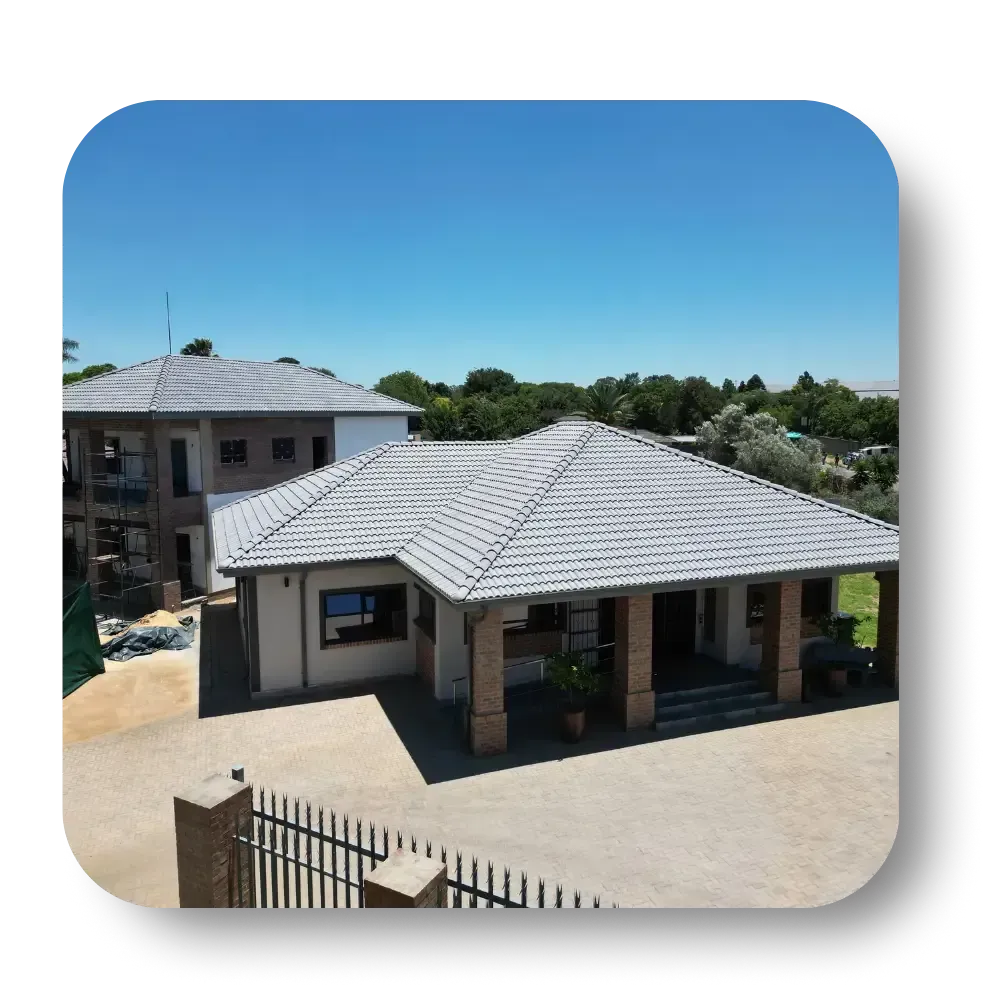 Two-story beige building with gray tiled roof under a blue sky.