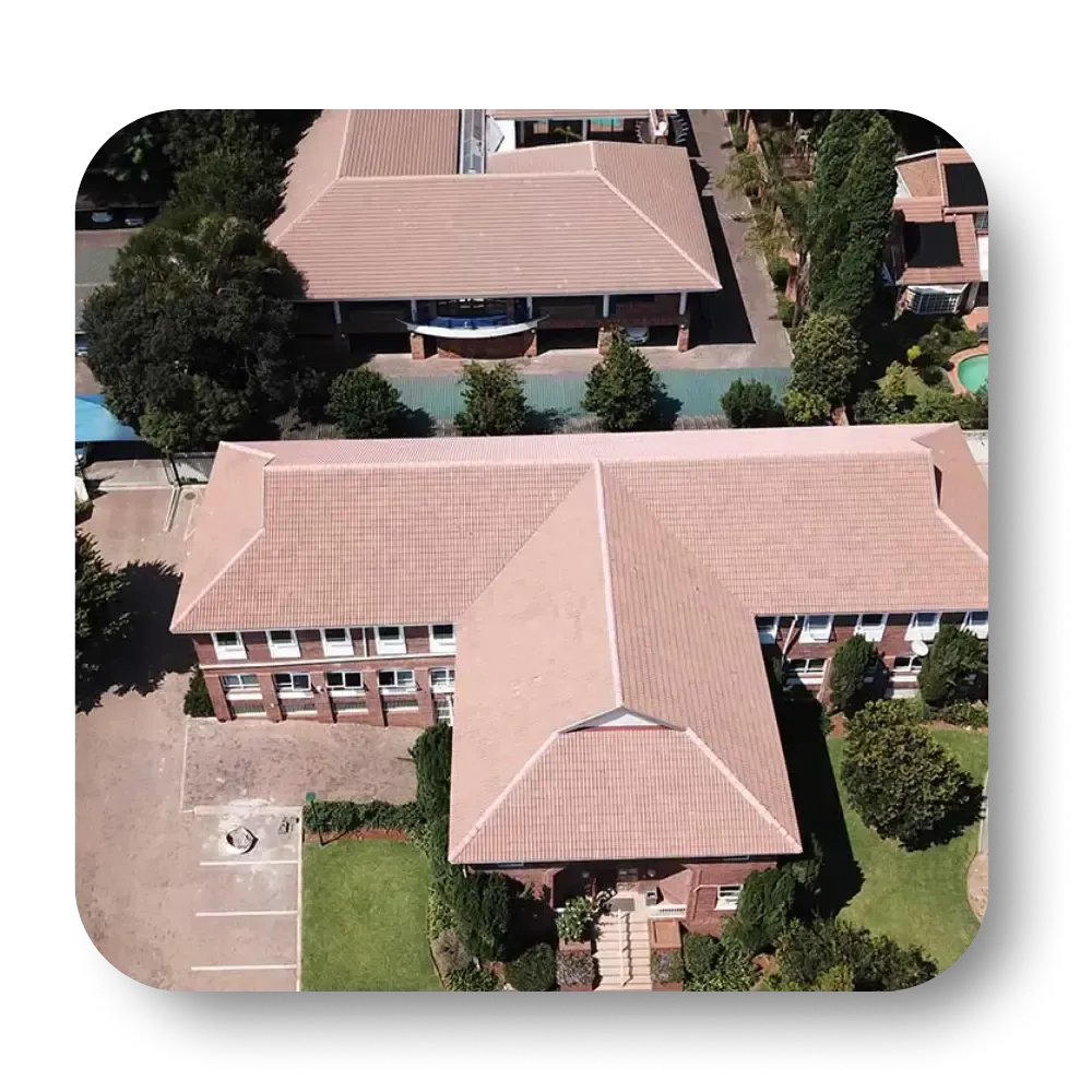 Aerial view of a brick building with a brown tiled roof, surrounded by trees and a small lawn.