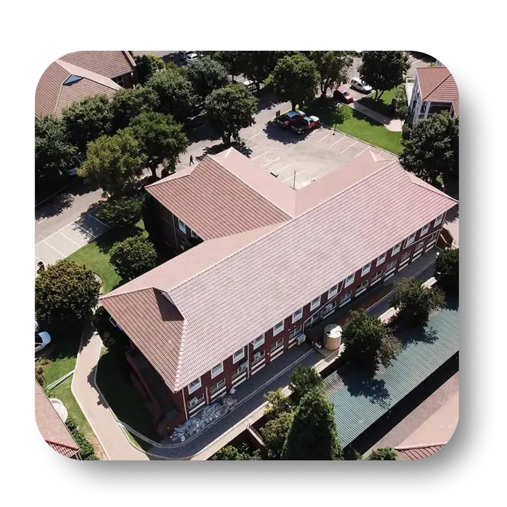 Aerial view of a brick school building with a brown tiled roof, surrounded by trees and parking.