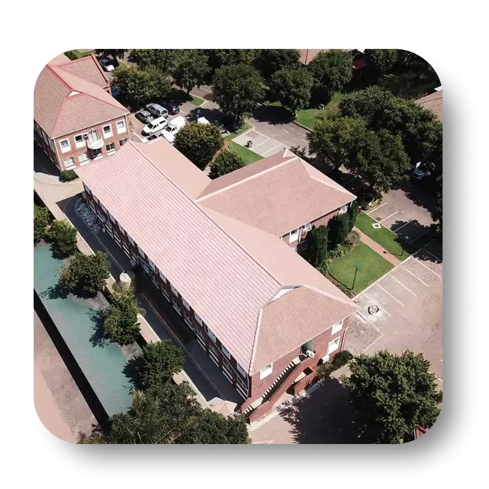 Aerial view of a brick building with a red roof surrounded by trees and parking.