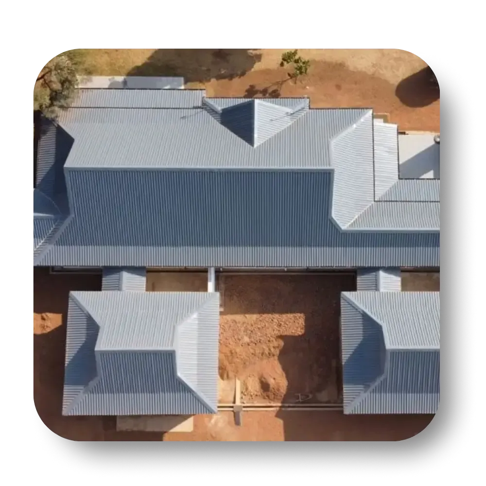 Aerial view of a building with a gray metal roof, brown earth, and surrounding trees.