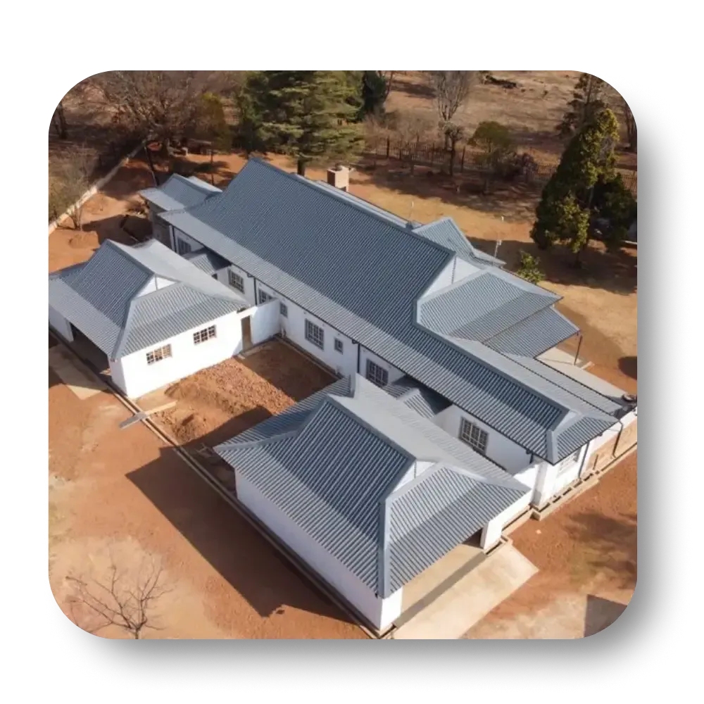 Aerial view of a white house with a dark gray roof, surrounded by trees and brown ground.