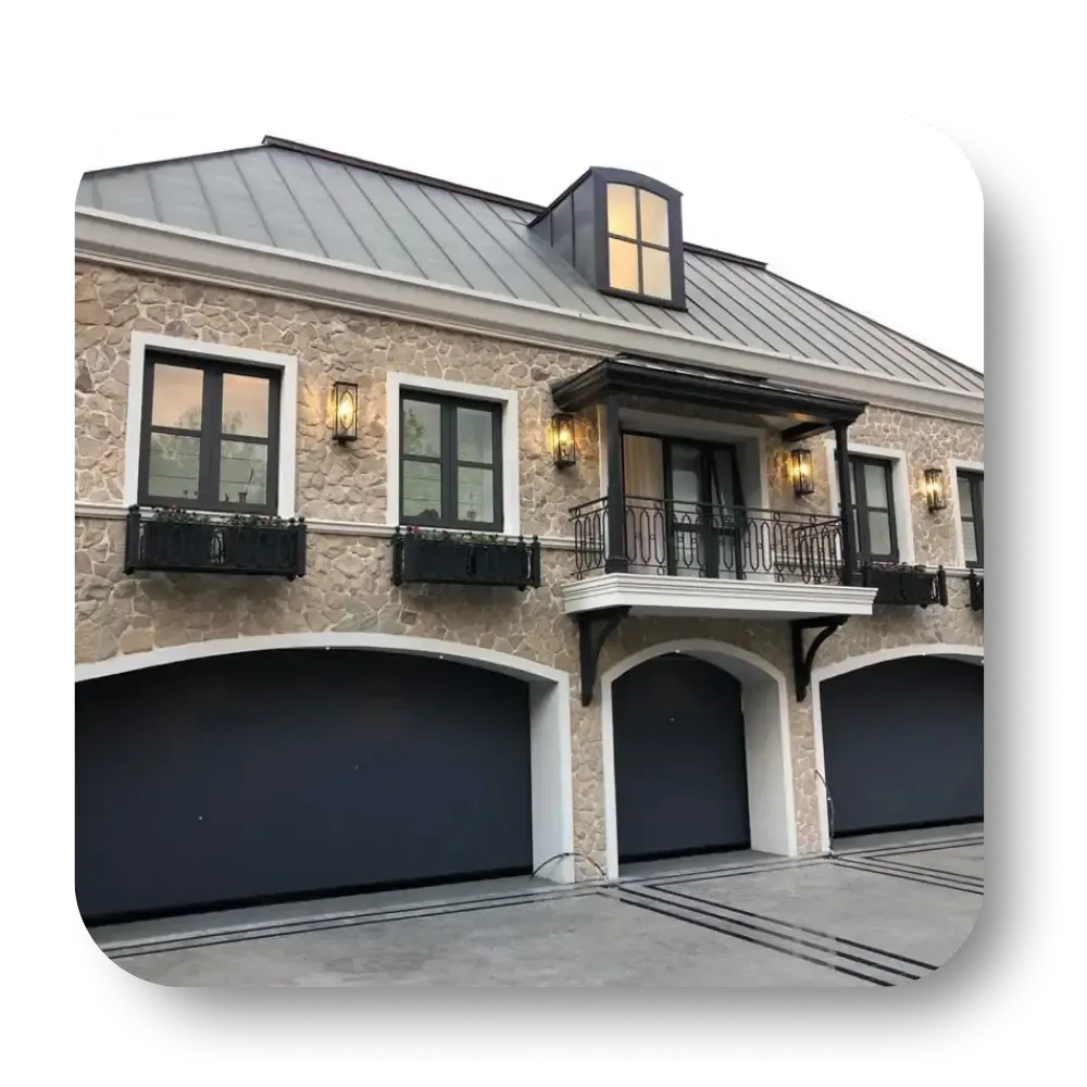 Three-car garage with gray doors, stone facade, black windows, and balcony.