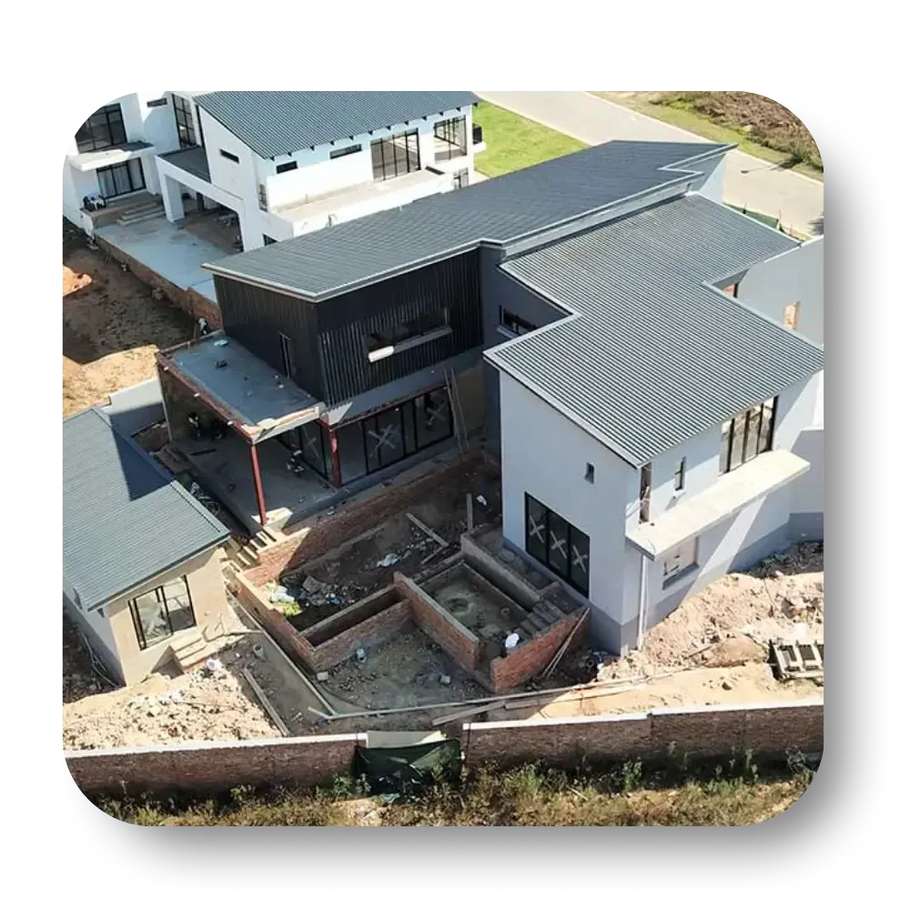 Aerial view of a modern house under construction with gray roof, brick foundations, and surrounding homes.