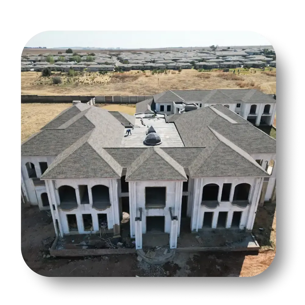 Unfinished mansion with gray roof, white walls, and multiple rectangular windows in a field.