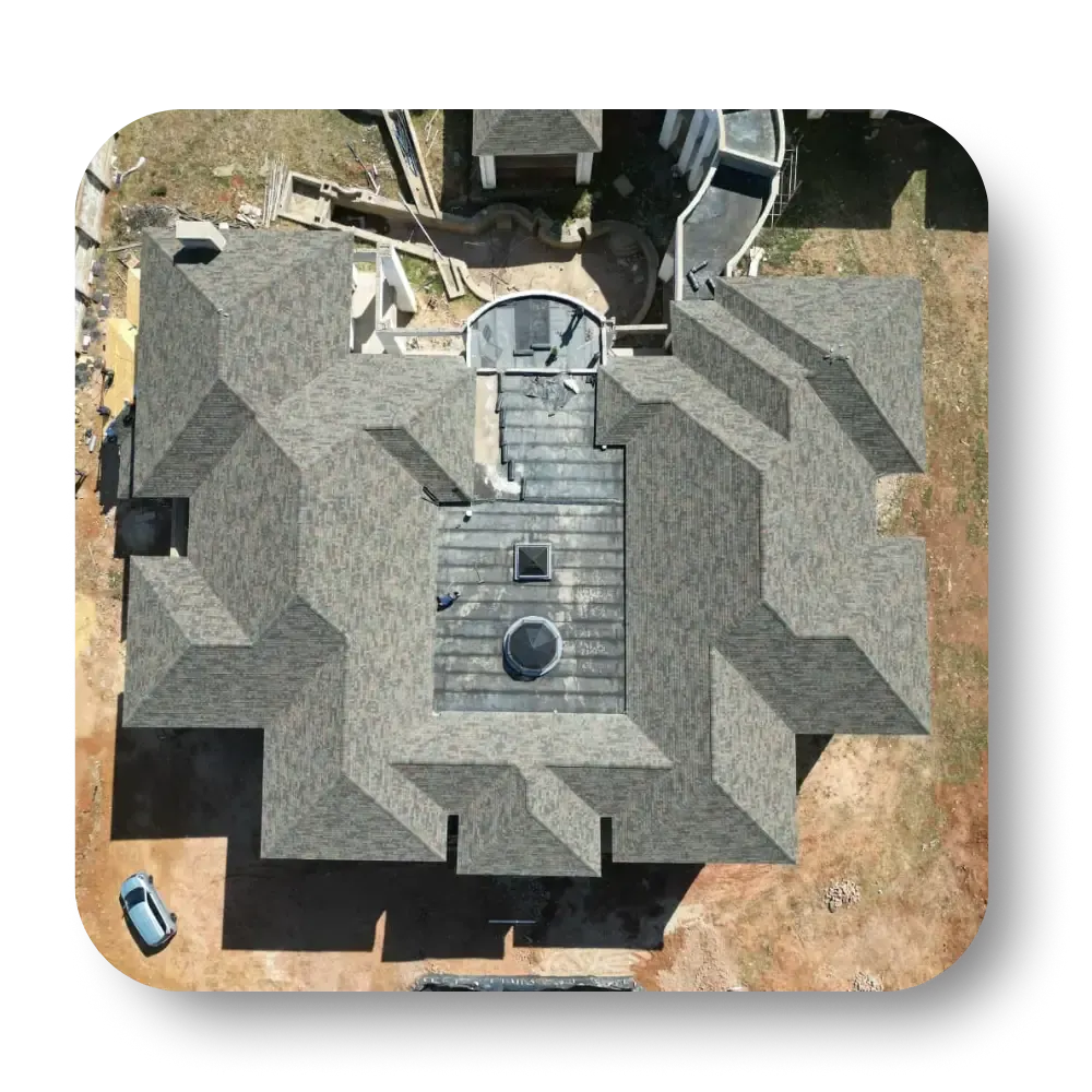 Aerial view of a large house with a gray shingle roof, surrounded by a brown yard; car parked in the corner.