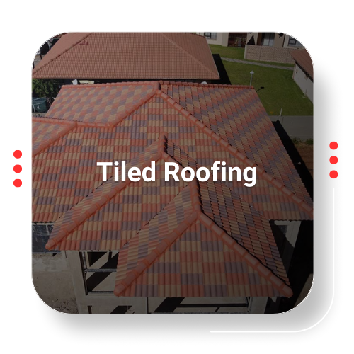 Tiled roofing on a house, aerial view. Multi-colored tiles, red trim, green lawn in background.