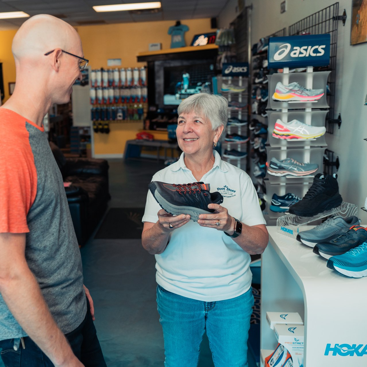 A man and woman are talking in a store with a sign that says asics