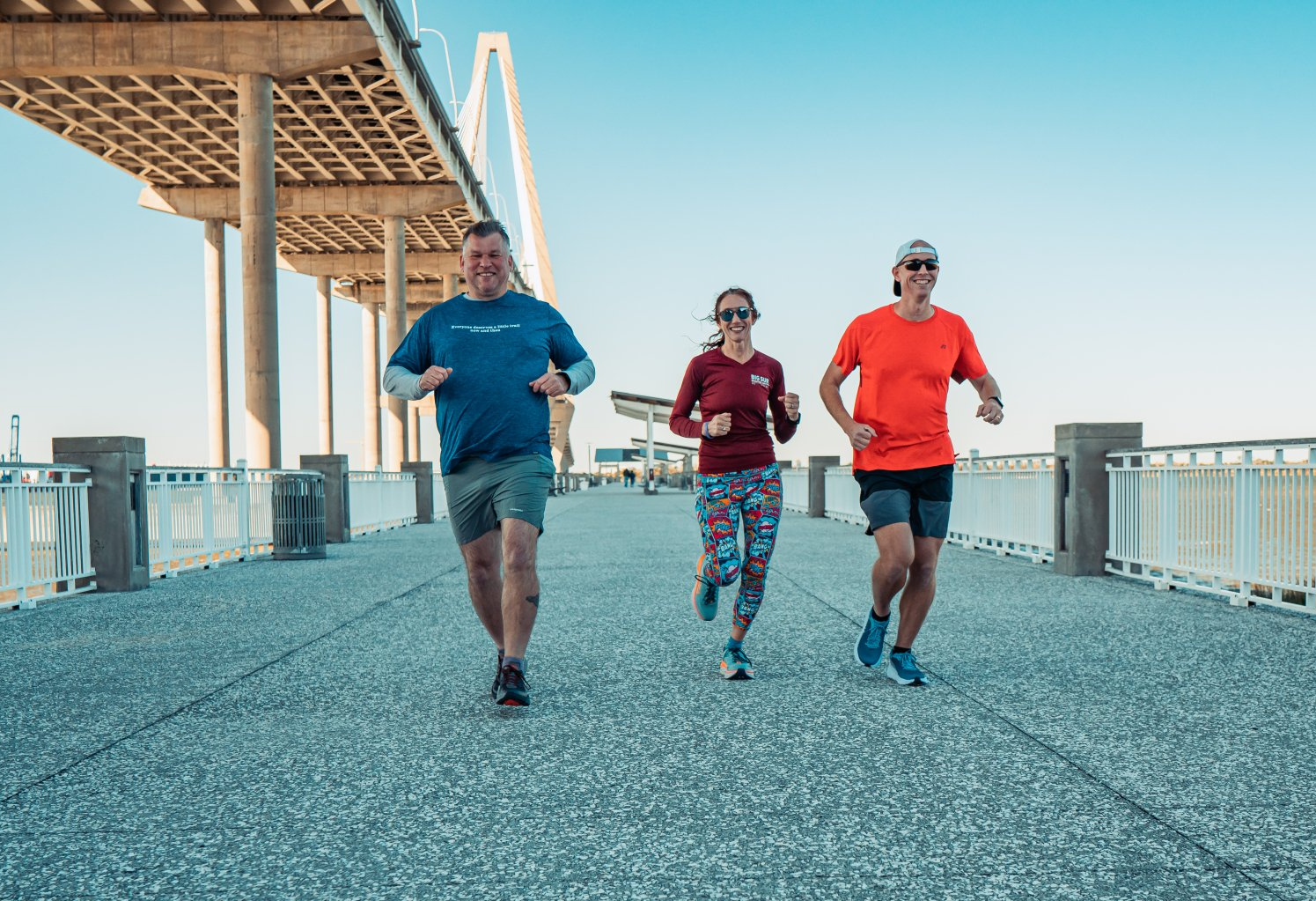 A group of people are running on a pier under a bridge.