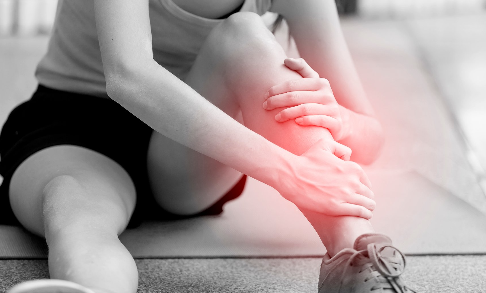 A woman is sitting on the floor holding her leg in pain.