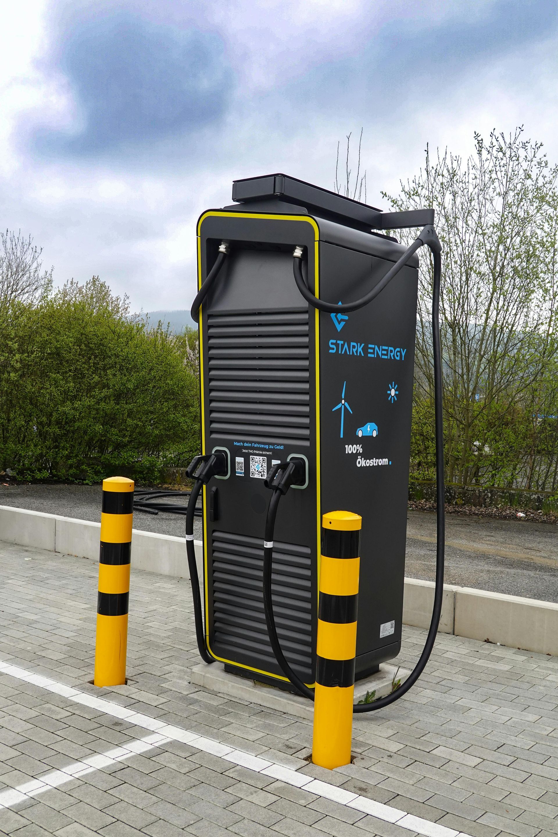 Electric vehicle charging station, black with yellow trim, two charging ports, safety bollards.
