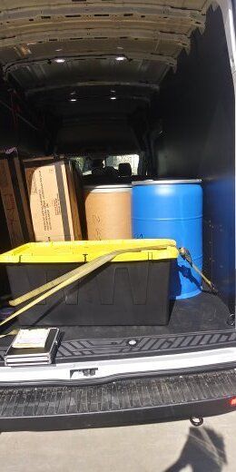 Inside of a van, there are boxes, barrels, and a toolbox.
