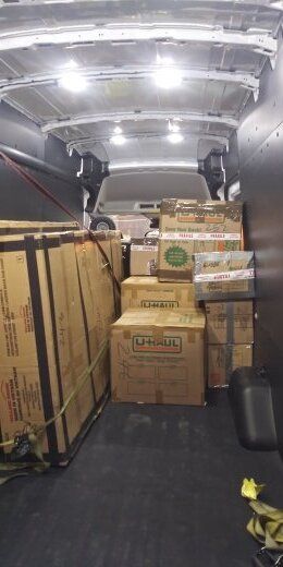 Interior of a cargo van filled with cardboard boxes, crates, and wooden panels.