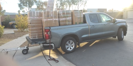 A gray pickup truck carrying boxes in its bed, a trailer attached, parked on a driveway.