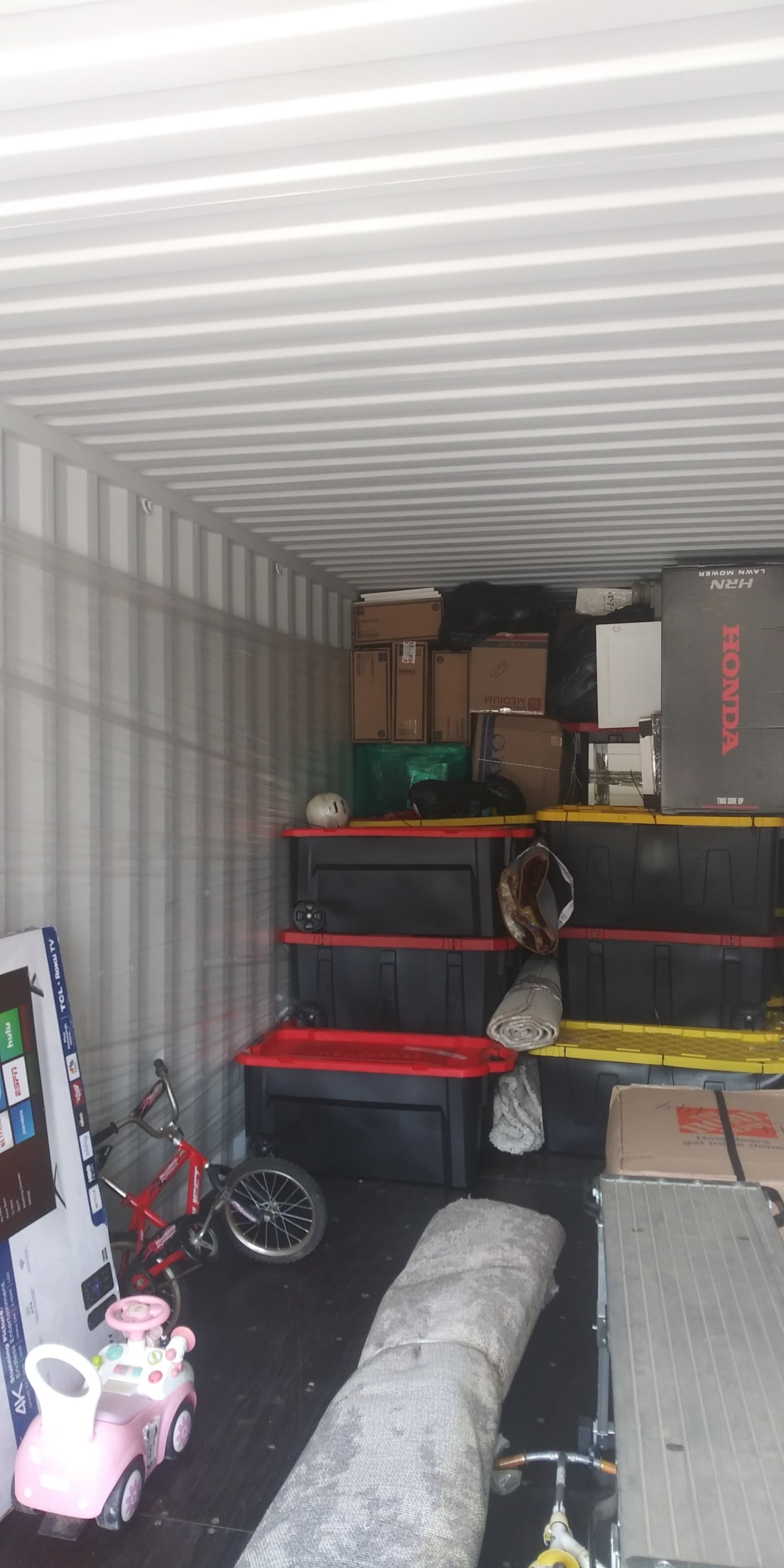Interior of a shipping container filled with various household items, including boxes, a rug, and a child's bicycle.