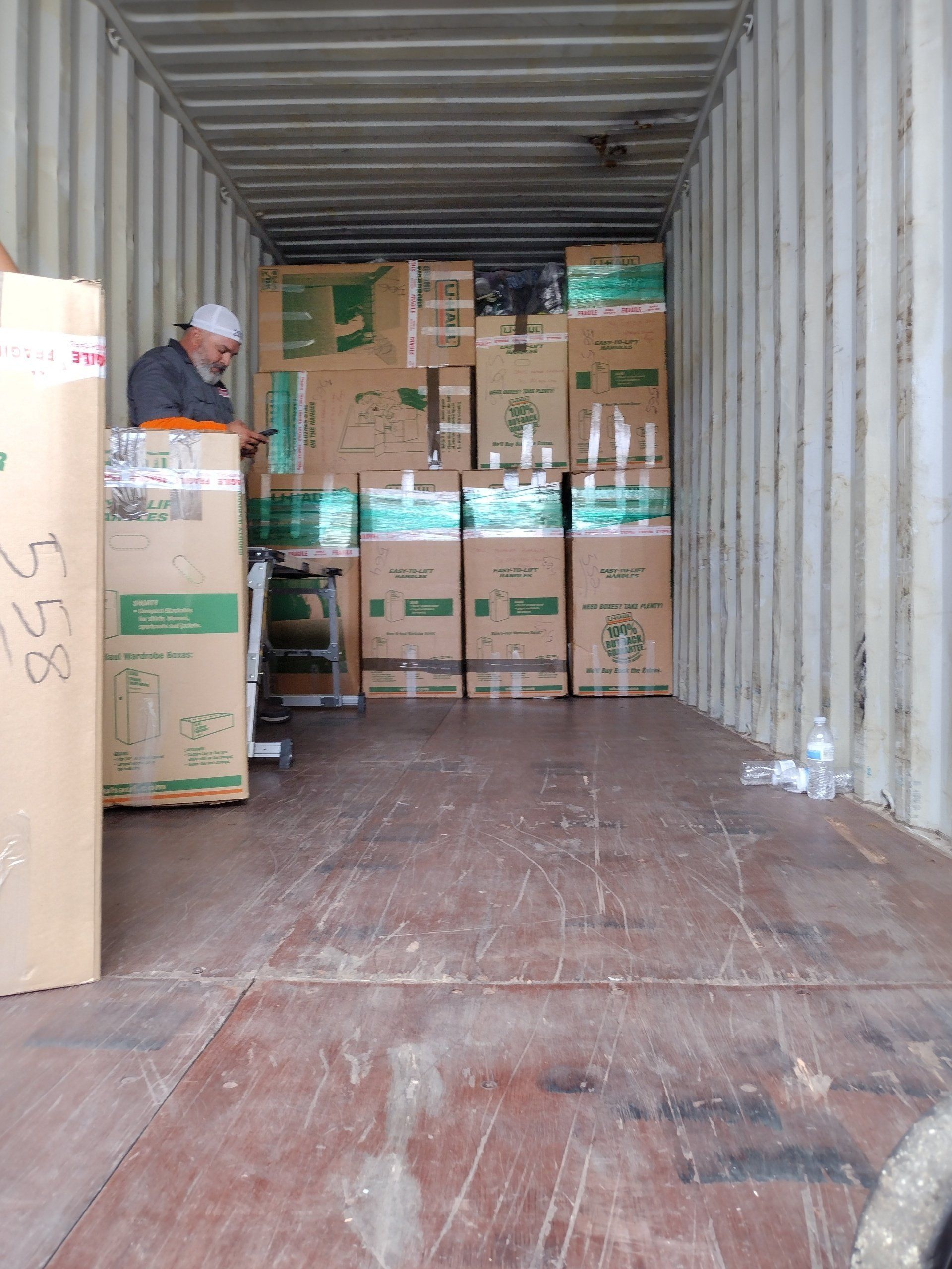 Man in a shipping container surrounded by stacked boxes. Wooden floor.