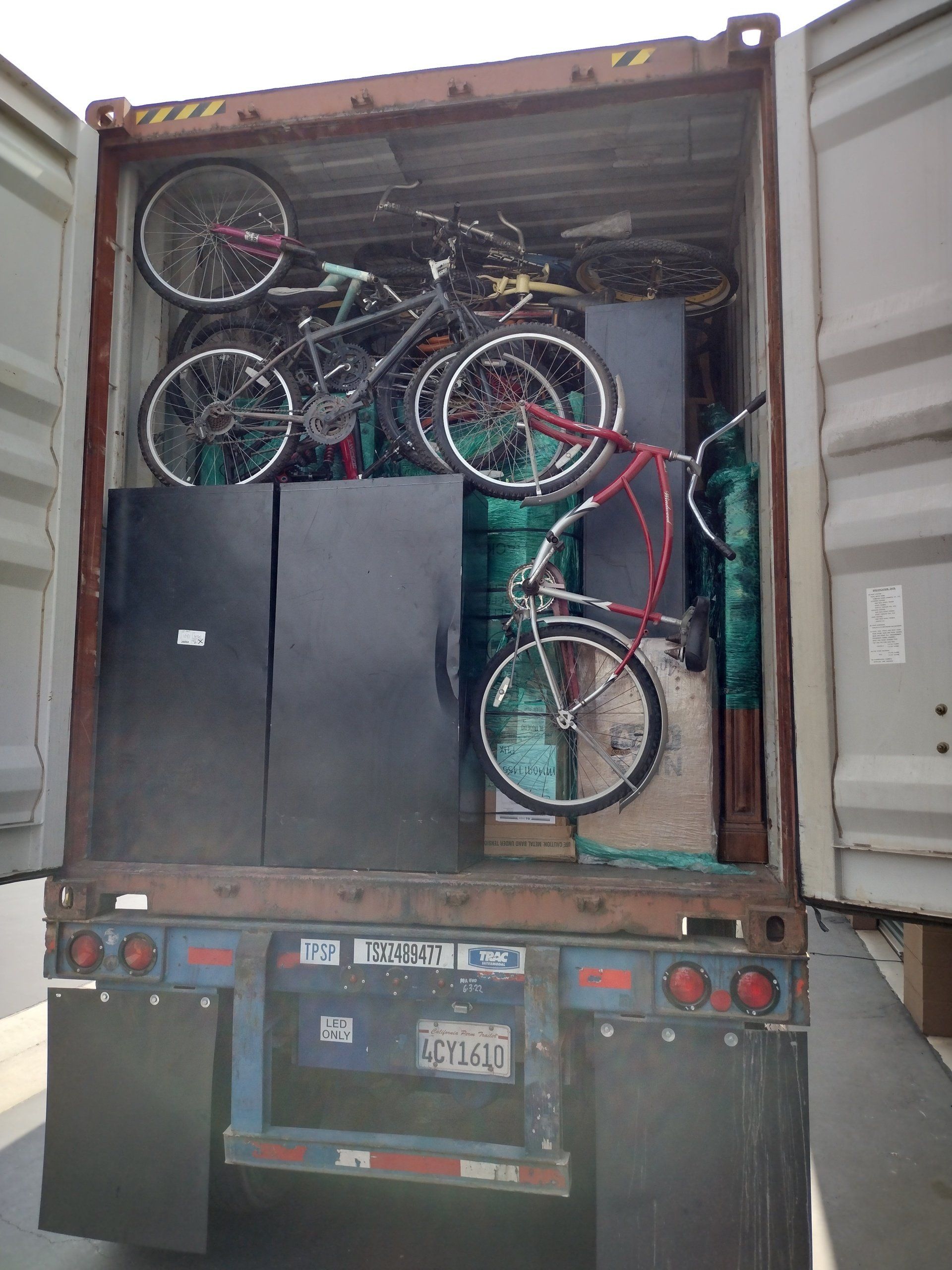Shipping container loaded with bicycles and two dark cabinets on a truck.