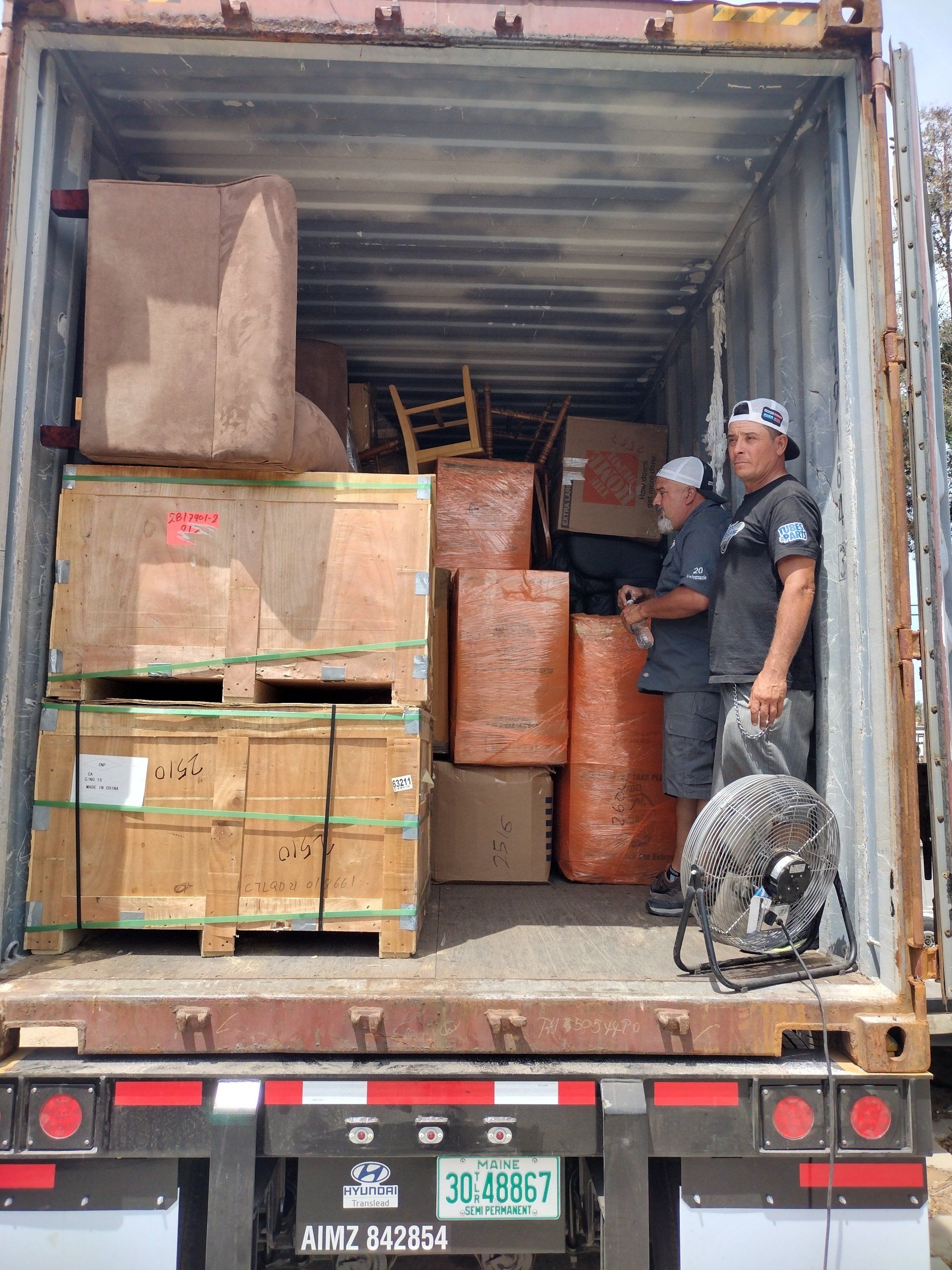Men loading a shipping container with furniture, boxes and packaged items.