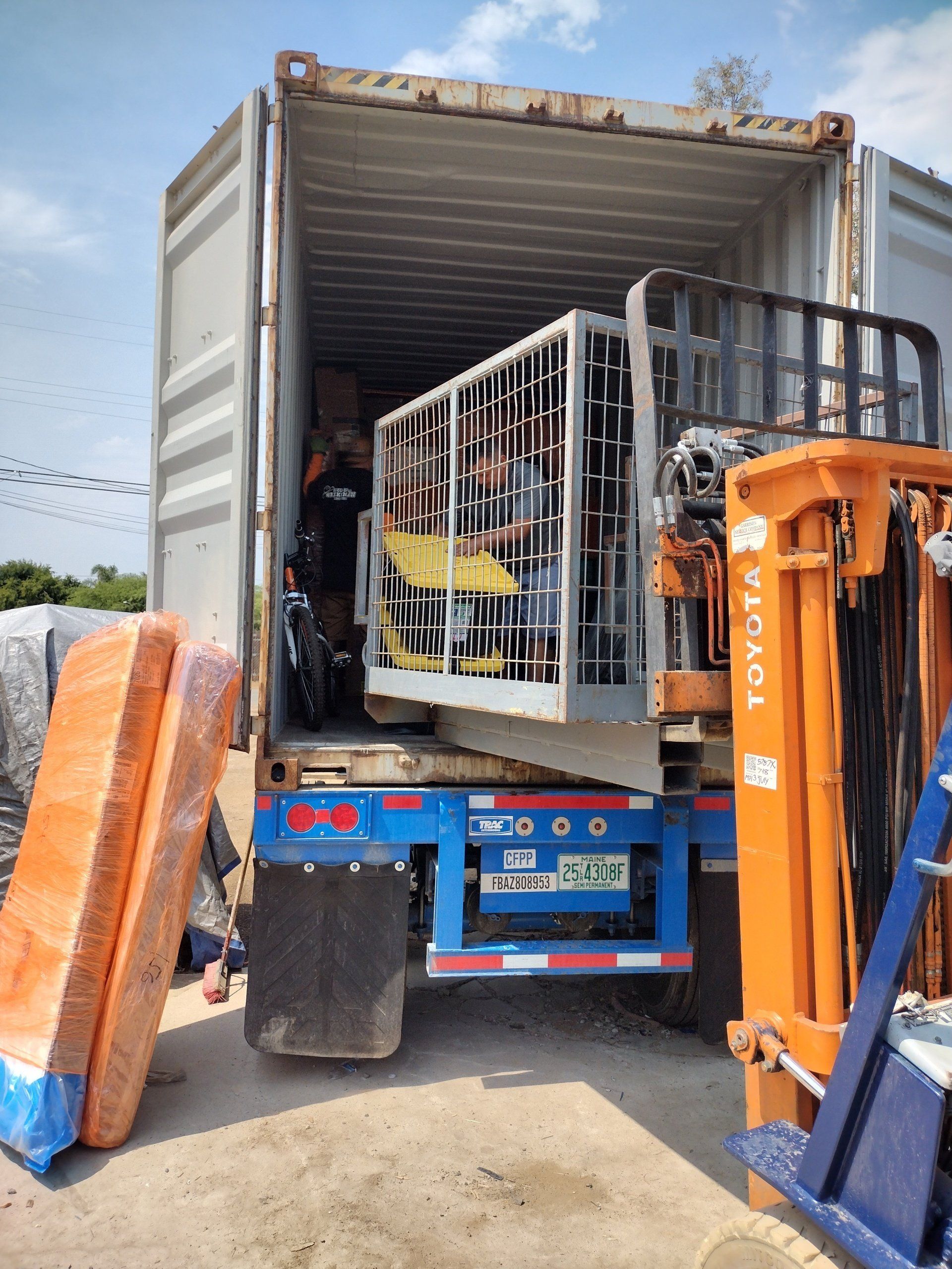 Forklift loading items, including chairs, into a shipping container on a truck.
