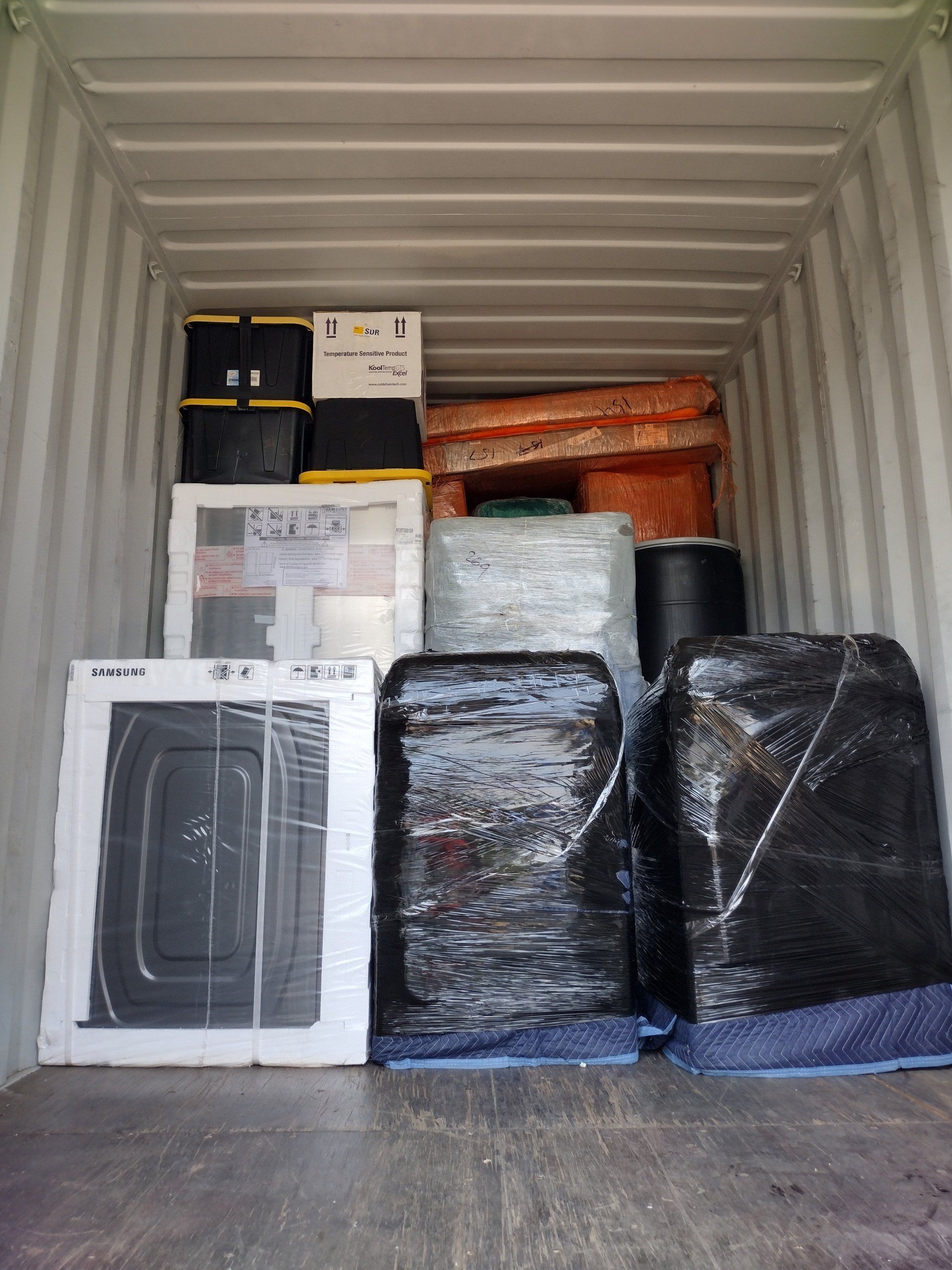 Shipping container filled with household items wrapped in plastic, ready for transport.